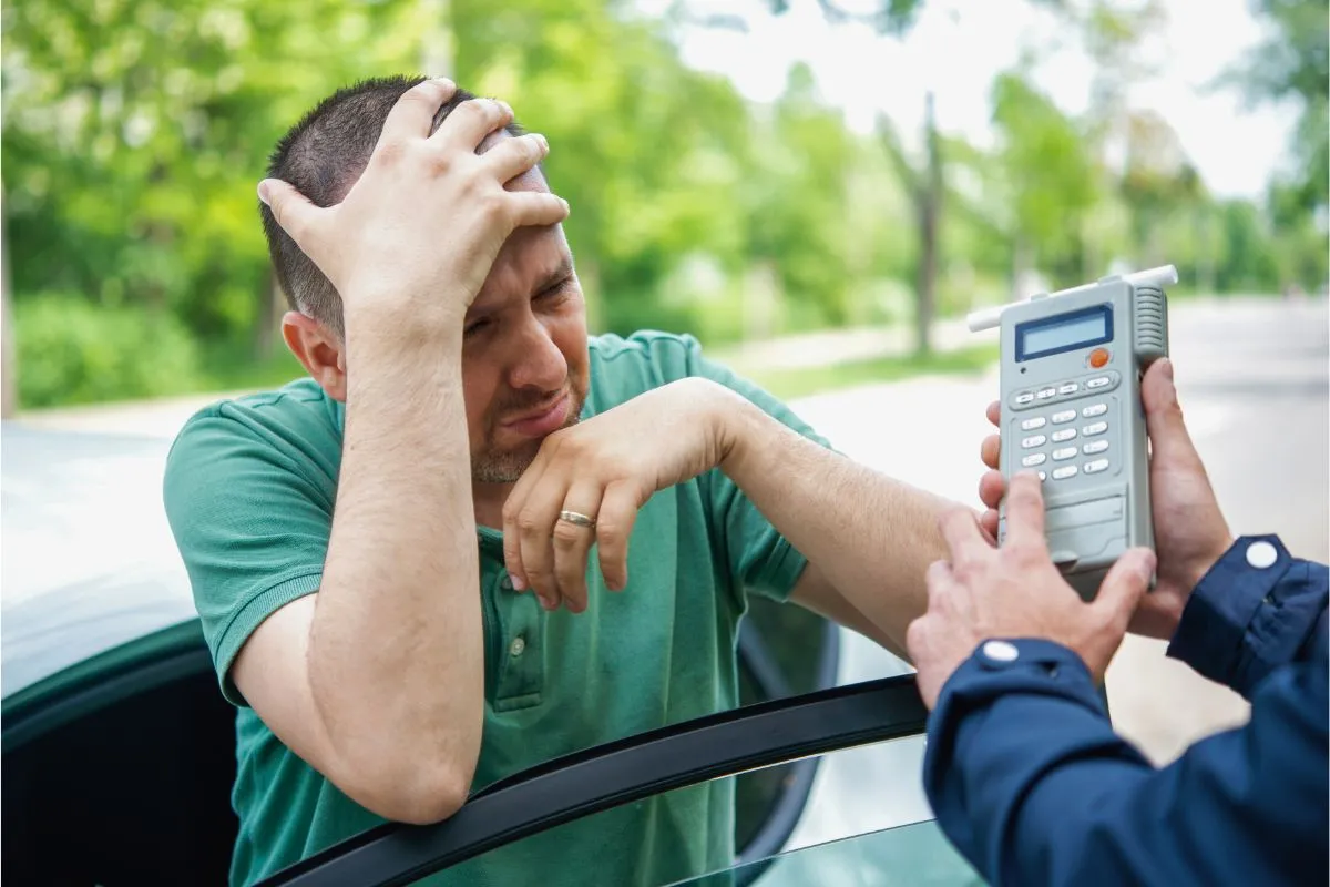Motorista frustrado ao lado do carro após resultado do teste do bafômetro que gerou multa